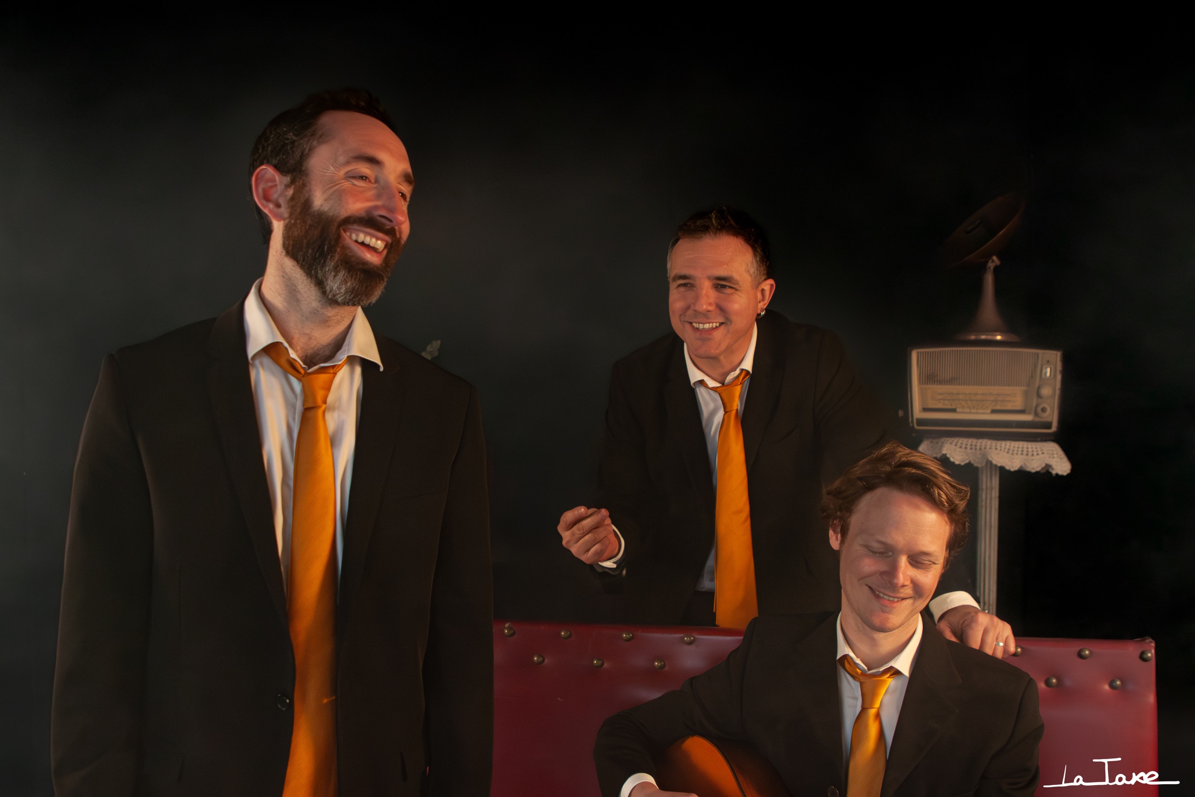 Les trois musiciens de My Favourite Swing, en costumes noirs et cravates cuivrées, réunis autour d’une guitare